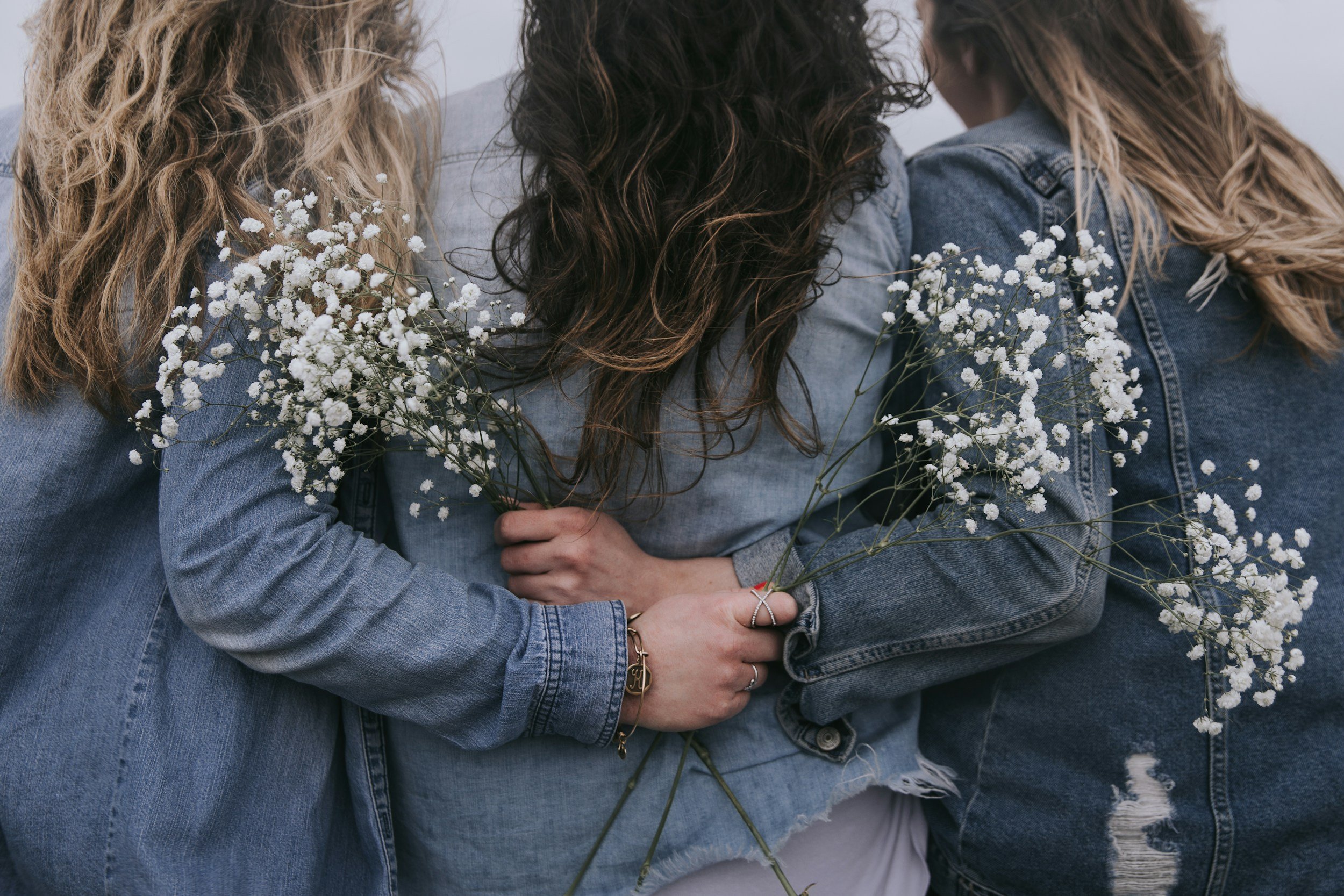 Three people in denim jackets holding white flowers.