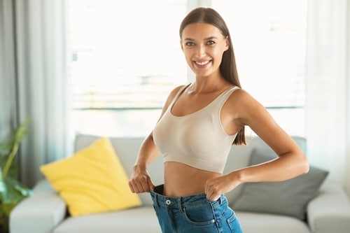 Woman smiling and showing loose jeans, symbolizing weight loss.