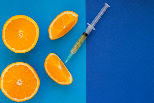 Vitamin shot syringe with orange slices on blue background.