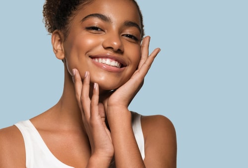 Smiling woman with clear skin, hands touching face.
