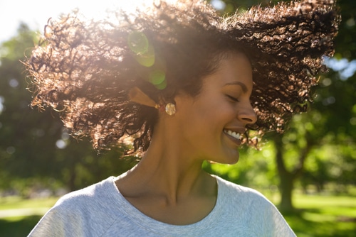 Woman enjoying a sunny day outdoors, smiling with eyes closed.