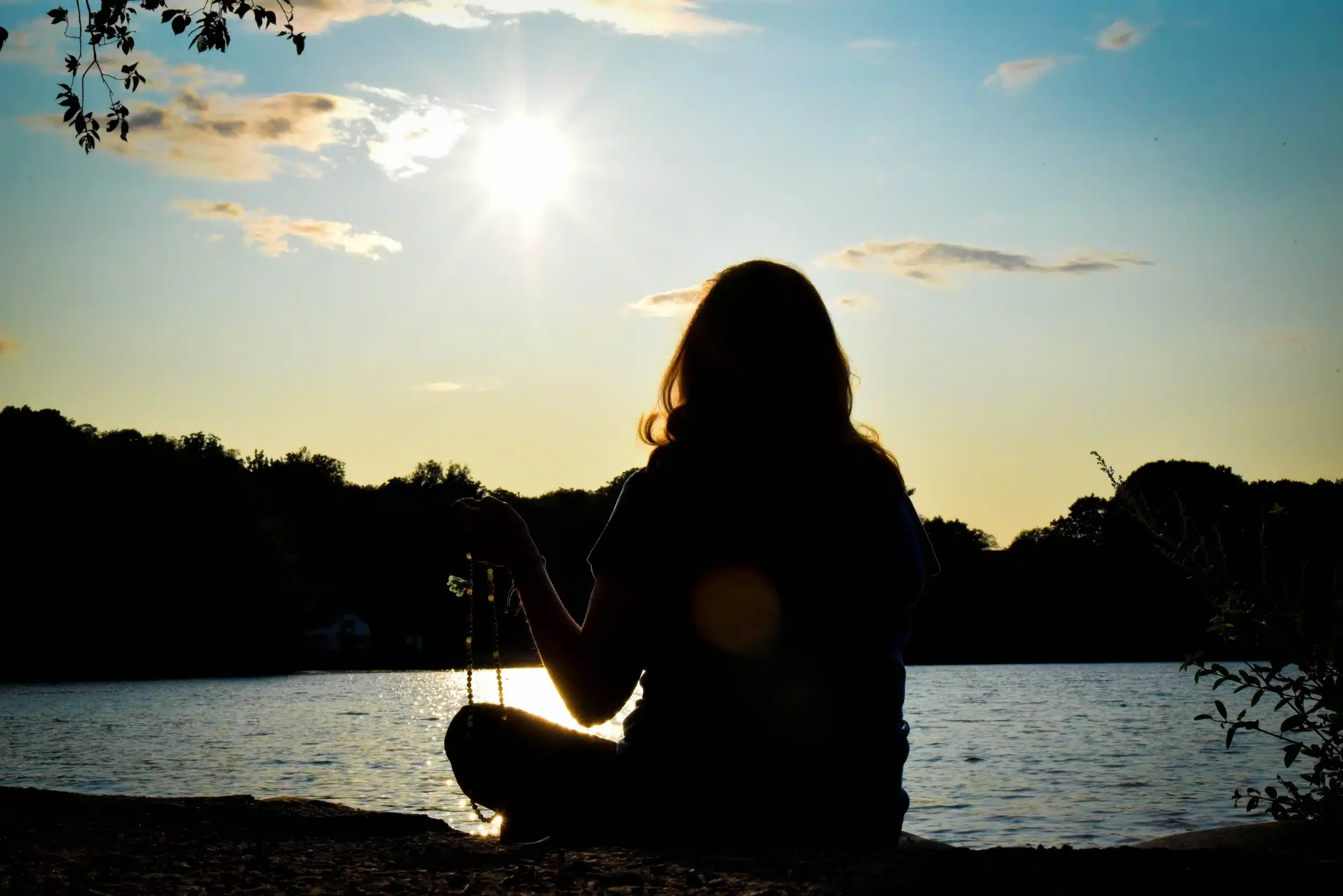 Silhouette of a person meditating by a lake at sunset.